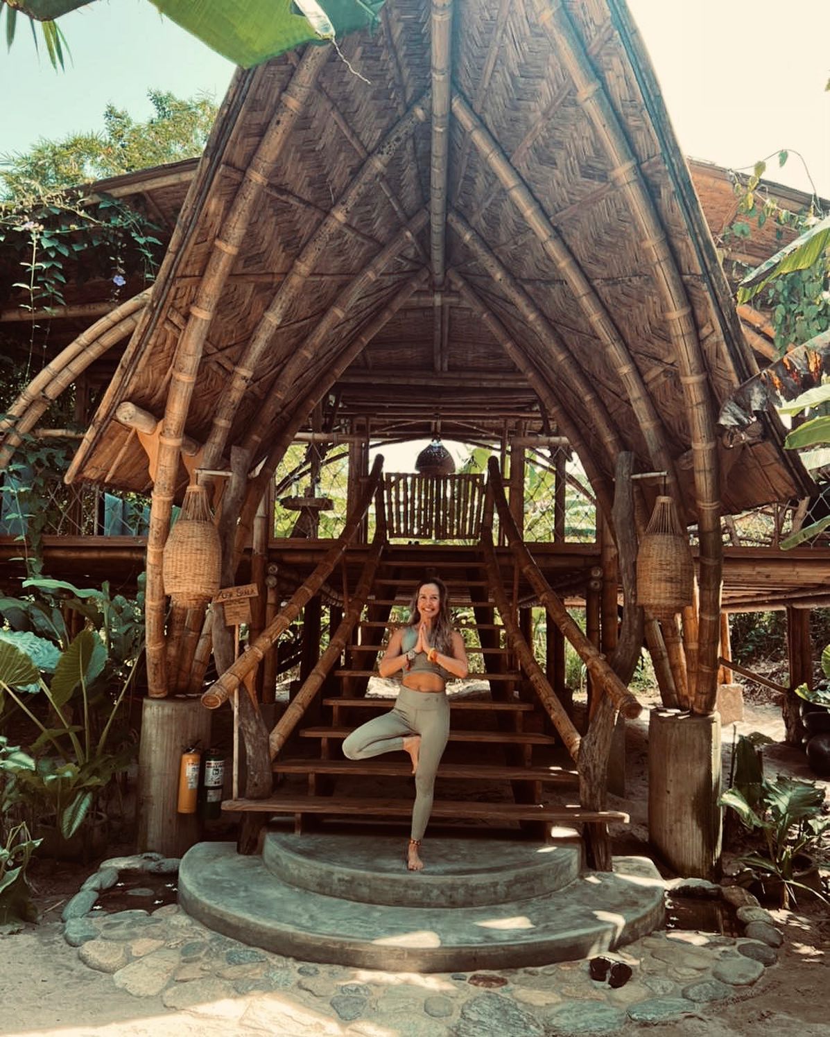 Woman practicing yoga in front of a wooden hut surrounded by nature